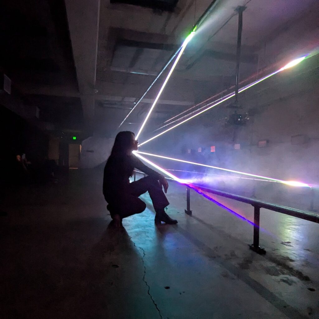 Silhouette of a girl kneeling with laser rays of light in the dark background